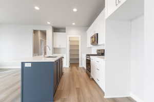 Kitchen with a center island with sink, appliances with stainless steel finishes, white cabinetry, light wood-type flooring, and sink