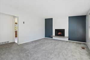 Unfurnished living room with carpet floors, a brick fireplace, and a textured ceiling