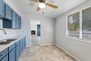 Kitchen with sink, a fireplace, ceiling fan, light tile patterned floors, and blue cabinetry