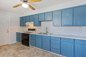 Kitchen with sink, light tile patterned floors, black gas range, ceiling fan, and blue cabinetry