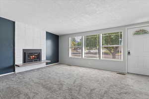 Unfurnished living room with carpet floors, a textured ceiling, and a brick fireplace