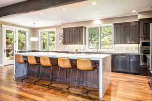 Kitchen with decorative backsplash, light wood-type flooring, beamed ceiling, a center island, and stainless steel appliances