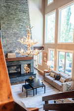 Living room featuring a high ceiling, hardwood / wood-style flooring, a stone fireplace, and a notable chandelier