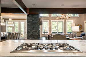 Kitchen with stainless steel gas stovetop, a notable chandelier, light stone counters, and a healthy amount of sunlight