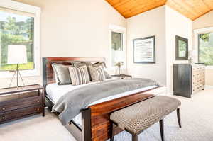 Bedroom with vaulted ceiling, wooden ceiling, and light colored carpet