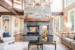 Living room with a wealth of natural light, an inviting chandelier, hardwood / wood-style floors, and a stone fireplace