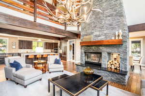 Living room featuring a towering ceiling, light wood-type flooring, an inviting chandelier, and a stone fireplace