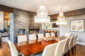 Dining area with beam ceiling, a chandelier, a stone fireplace, and dark hardwood / wood-style floors