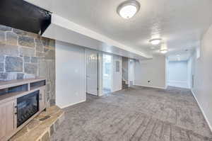 Basement with a stone fireplace, a textured ceiling, and carpet flooring