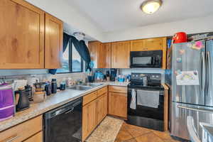 Kitchen with sink, decorative backsplash, light tile patterned floors, and black appliances