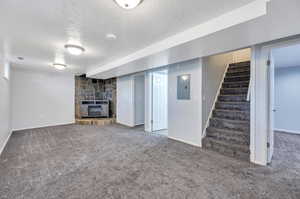 Basement with a fireplace, carpet floors, electric panel, and a textured ceiling