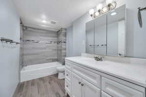 Full bathroom with toilet, vanity, wood-type flooring, a textured ceiling, and tiled shower / bath combo