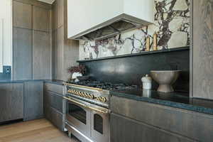 Kitchen featuring custom range hood, dark brown cabinets, decorative backsplash, light hardwood / wood-style floors, and double oven range