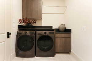 Clothes washing area with washing machine and dryer, cabinets, and light tile patterned floors