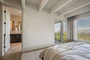 Bedroom with beam ceiling, light parquet floors, ensuite bath, and access to exterior