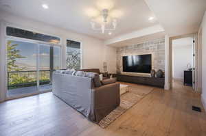 Living room with light wood-type flooring, an inviting chandelier, a tray ceiling, and a stone fireplace