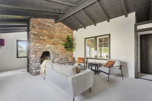 Carpeted living room with wood ceiling, beam ceiling, high vaulted ceiling, and a stone fireplace