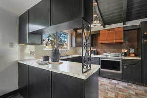 Kitchen with sink, custom exhaust hood, decorative backsplash, stove, and kitchen peninsula