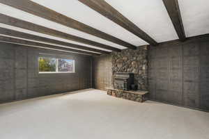 Unfurnished living room with carpet floors, beamed ceiling, a wood stove, a fireplace, and wooden walls