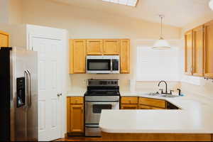 Kitchen with hanging light fixtures, vaulted ceiling, sink, kitchen peninsula, and stainless steel appliances