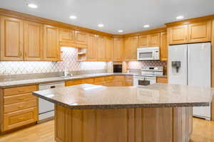 Kitchen with light wood-type flooring, a kitchen island, decorative backsplash, and white appliances