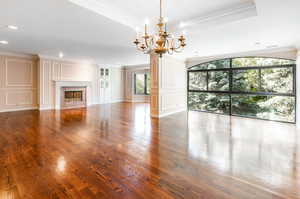 Unfurnished living room with ornamental molding, an inviting chandelier, a premium fireplace, and wood-type flooring