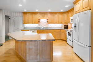 Kitchen with sink, decorative backsplash, light hardwood / wood-style floors, and white appliances