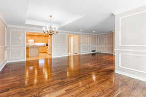 Unfurnished living room with light hardwood / wood-style floors, crown molding, a notable chandelier, and a tray ceiling