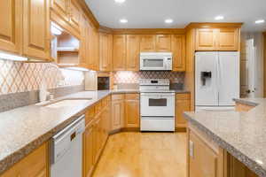 Kitchen featuring light hardwood / wood-style floors, sink, tasteful backsplash, and white appliances