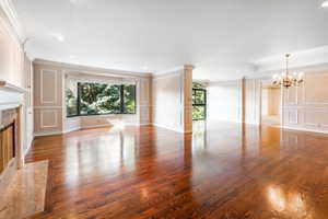 Unfurnished living room featuring hardwood / wood-style floors, a chandelier, a raised ceiling, crown molding, and a high end fireplace