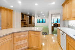 Kitchen with dishwasher, light colored carpet, light brown cabinets, and light stone counters