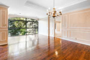 Unfurnished room with a tray ceiling, hardwood / wood-style floors, ornamental molding, and a chandelier