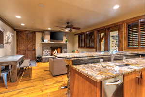 Kitchen featuring ceiling fan, light wood-type flooring, light stone countertops, sink, and a fireplace