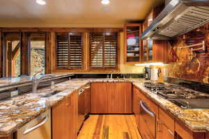 Kitchen with light wood-type flooring, sink, wall chimney range hood, and light stone countertops