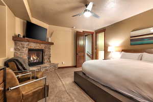 Carpeted bedroom with ceiling fan, a stone fireplace, and a textured ceiling