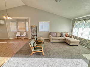 Living room featuring lofted ceiling, a healthy amount of sunlight, hardwood / wood-style flooring, and a chandelier