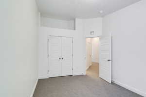 Unfurnished bedroom featuring a textured ceiling, light colored carpet, and a closet