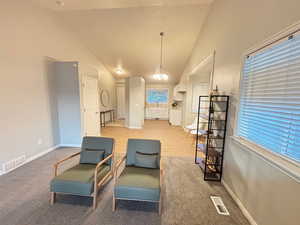 Living area with high vaulted ceiling, light colored carpet, and a chandelier