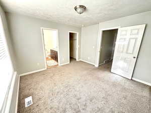 Unfurnished bedroom featuring a spacious closet, light colored carpet, a closet, ensuite bathroom, and a textured ceiling