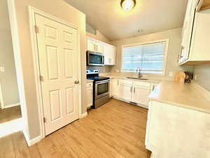 Kitchen featuring appliances with stainless steel finishes, light hardwood / wood-style floors, sink, lofted ceiling, and white cabinets