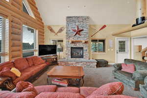 Carpeted living room featuring log walls, a high ceiling, and a stone fireplace