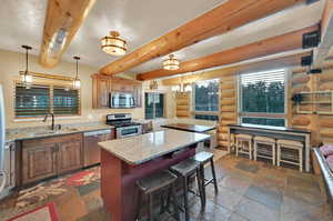 Kitchen featuring appliances with stainless steel finishes, decorative light fixtures, sink, light stone countertops, and a kitchen island