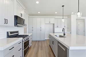 Kitchen featuring stainless steel appliances, light wood finished floors, decorative backsplash, a center island with sink, and light stone countertops