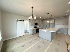 Kitchen with gray cabinets, a chandelier, a center island with sink, a barn door, and recessed lighting