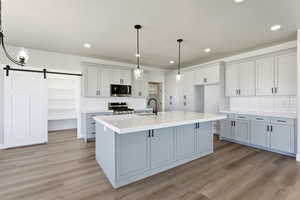 Kitchen featuring a barn door, light wood-type flooring, stainless steel appliances, an island with sink, and two tone cabinets