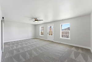 Spare room featuring a barn door, a ceiling fan, and light colored carpet