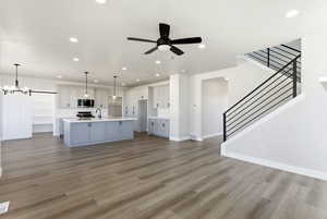 Unfurnished living room featuring a ceiling fan, light wood-style floors, and a chandelier