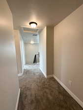 Hall with an upstairs landing, attic access, dark carpet, and a textured ceiling