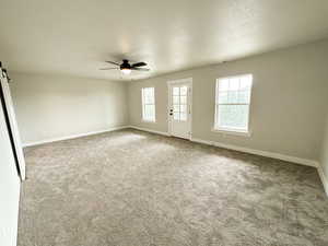 Carpeted empty room featuring a barn door, healthy amount of natural light, a textured ceiling, and ceiling fan