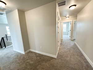 Hall with carpet flooring, a textured ceiling, an upstairs landing, and attic access